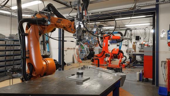 Figure 1: TWI's two robot LMD systems. Pictured left, recently installed Kuka robot with Precitec’s new coaxial wire LMD. Pictured right, Reis robot with powder LMD. Both using the same 5.3kW Trumpf disc laser