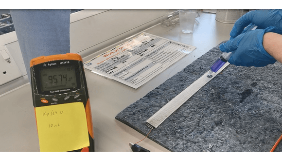 Figure 1. Example of hydraulic test. The Wrapsense sensor (white) is laid over the spill blanket and connected to the multimeter using clamps. A reading of 95.74 kOhm is displayed