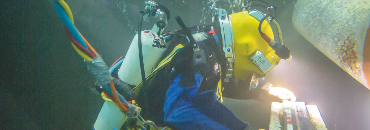 Commercial diver in a yellow helmet carrying out underwater inspection on a subsea structure