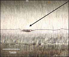 c) Optical micrograph taken directly from specimen 03 just before it failed, showing the initiation site for crack TA-1.